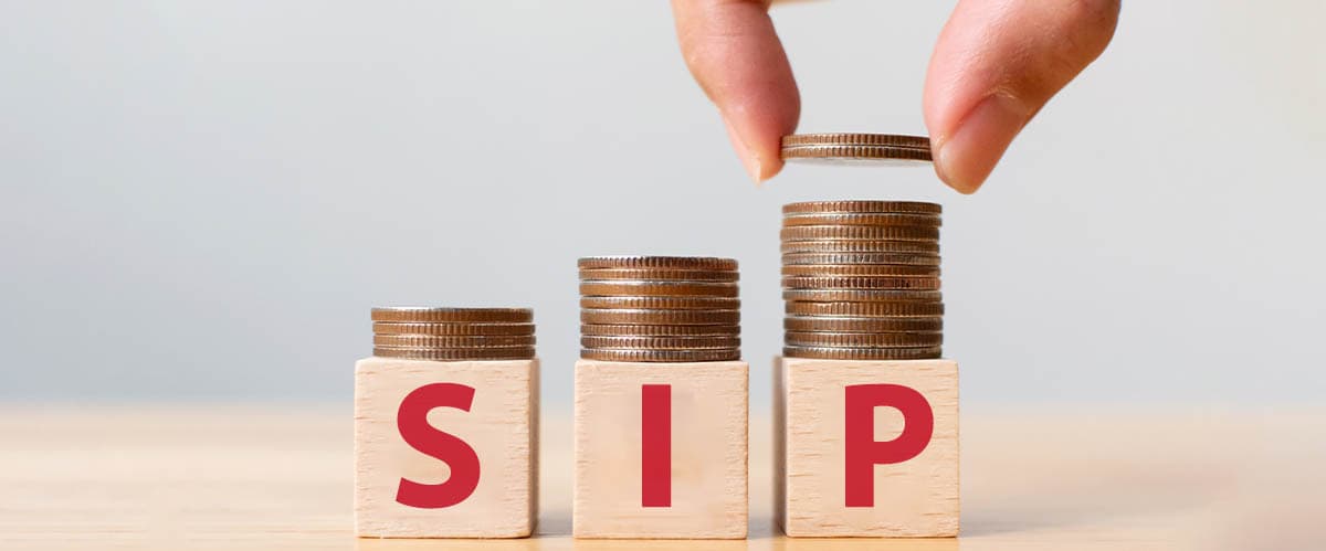 Hand placing coins on growing stacks above SIP blocks, representing systematic investment planning, wealth creation, and long-term mutual fund investing.